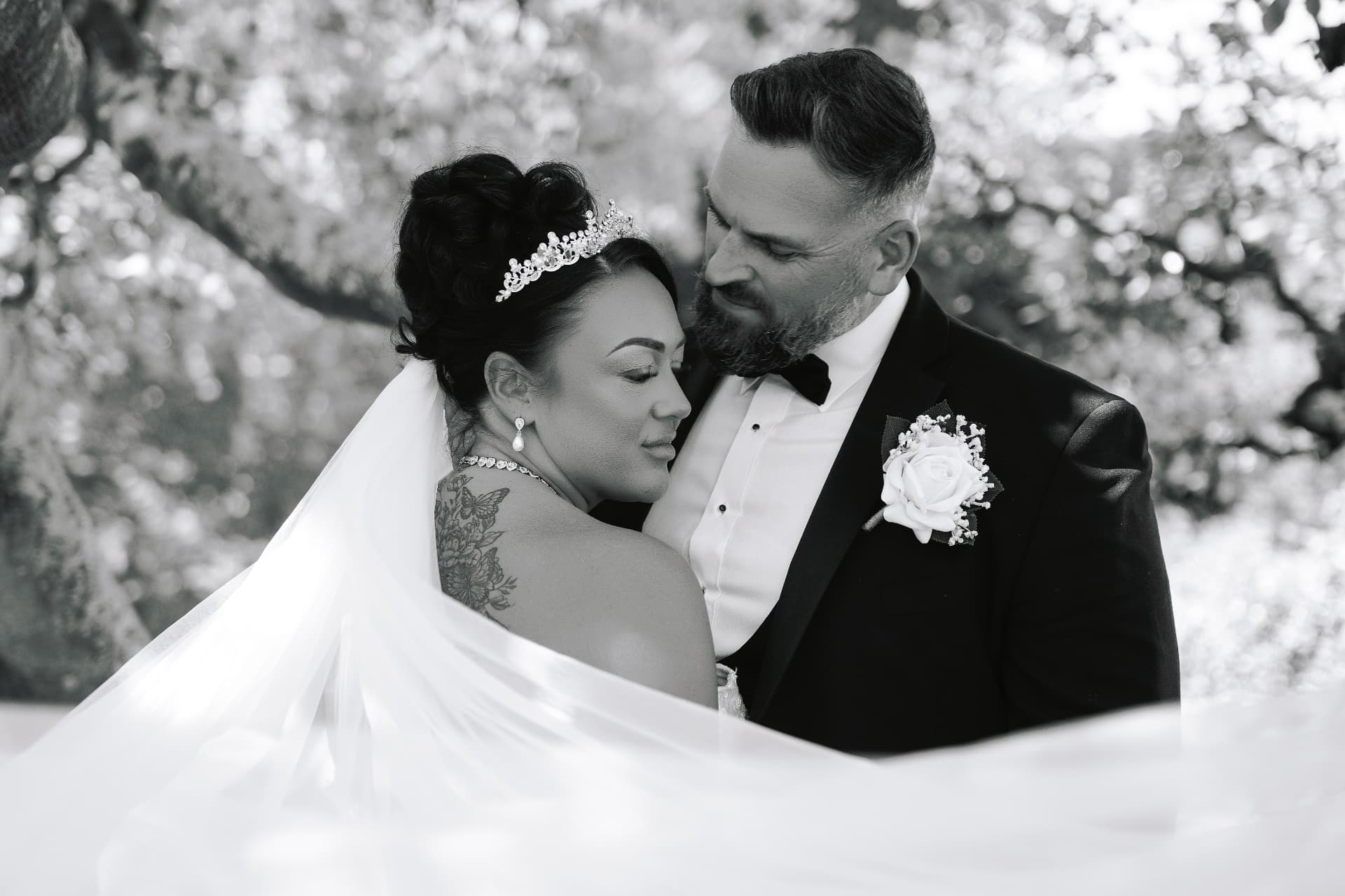 Bride and groom embracing beneath the trees in black and white