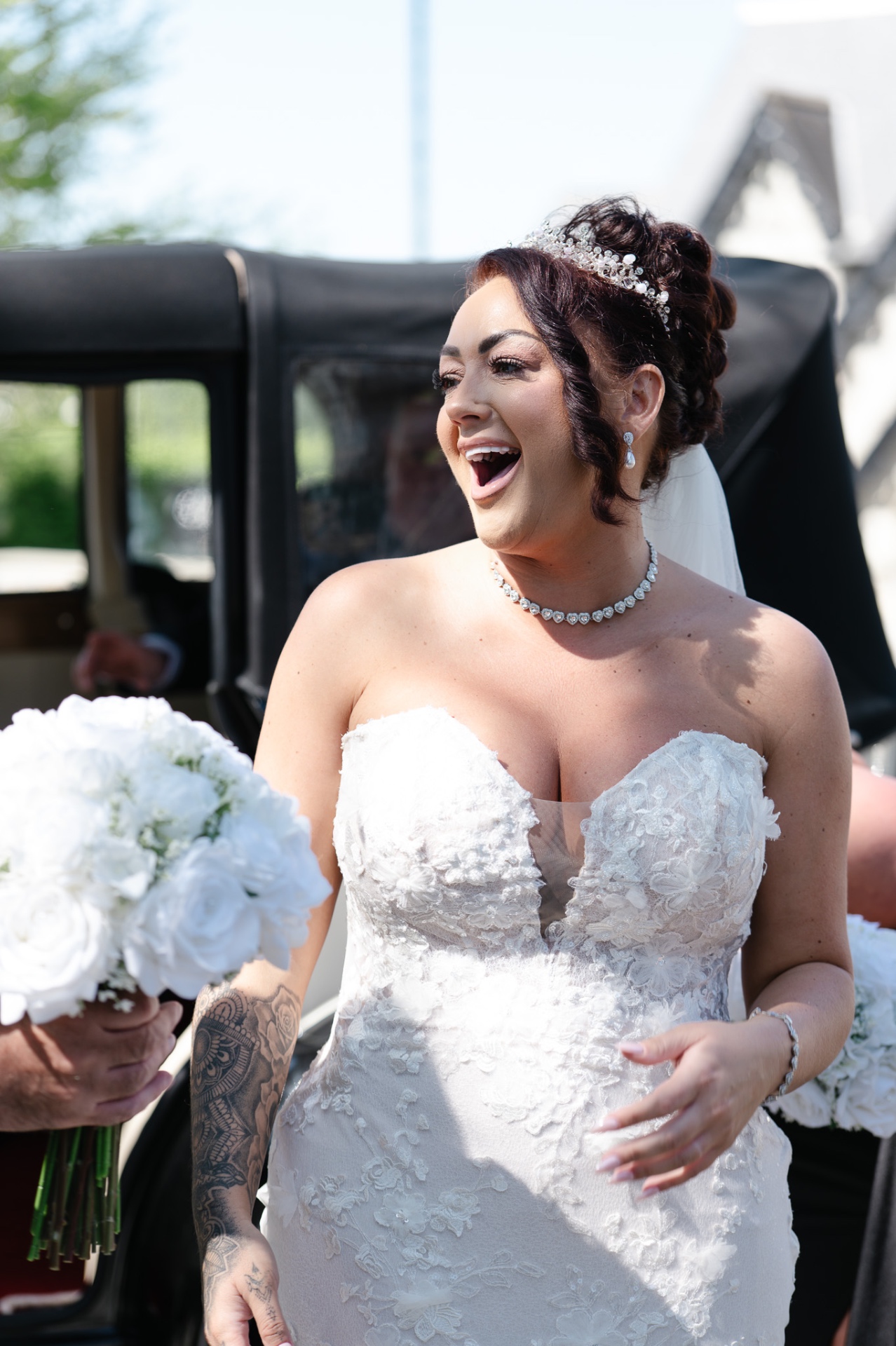 Bride laughing joyfully beside a vintage wedding car