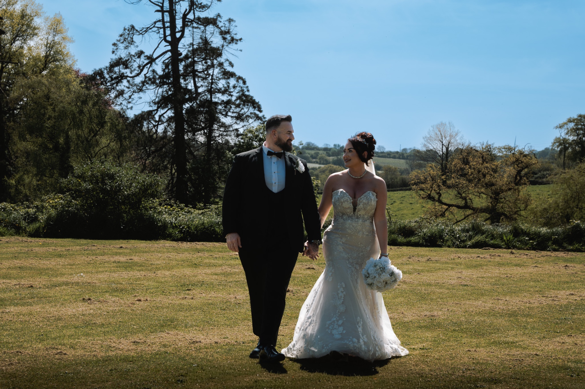 Bride and groom walking hand in hand through a sunny meadow