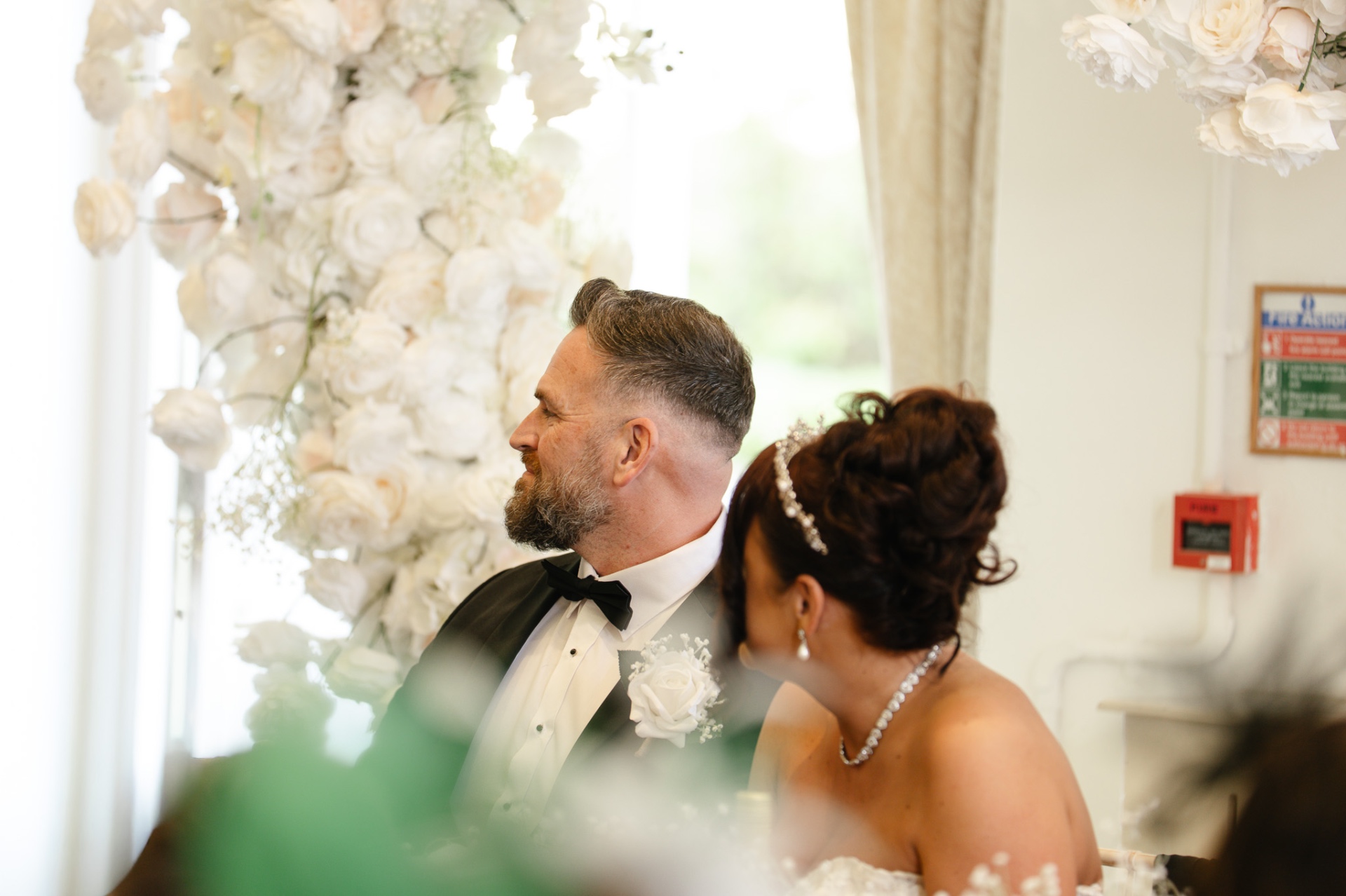 Tender candid moment between bride and groom during the ceremony, framed by white florals, wedding photography Worcestershire & Midlands
