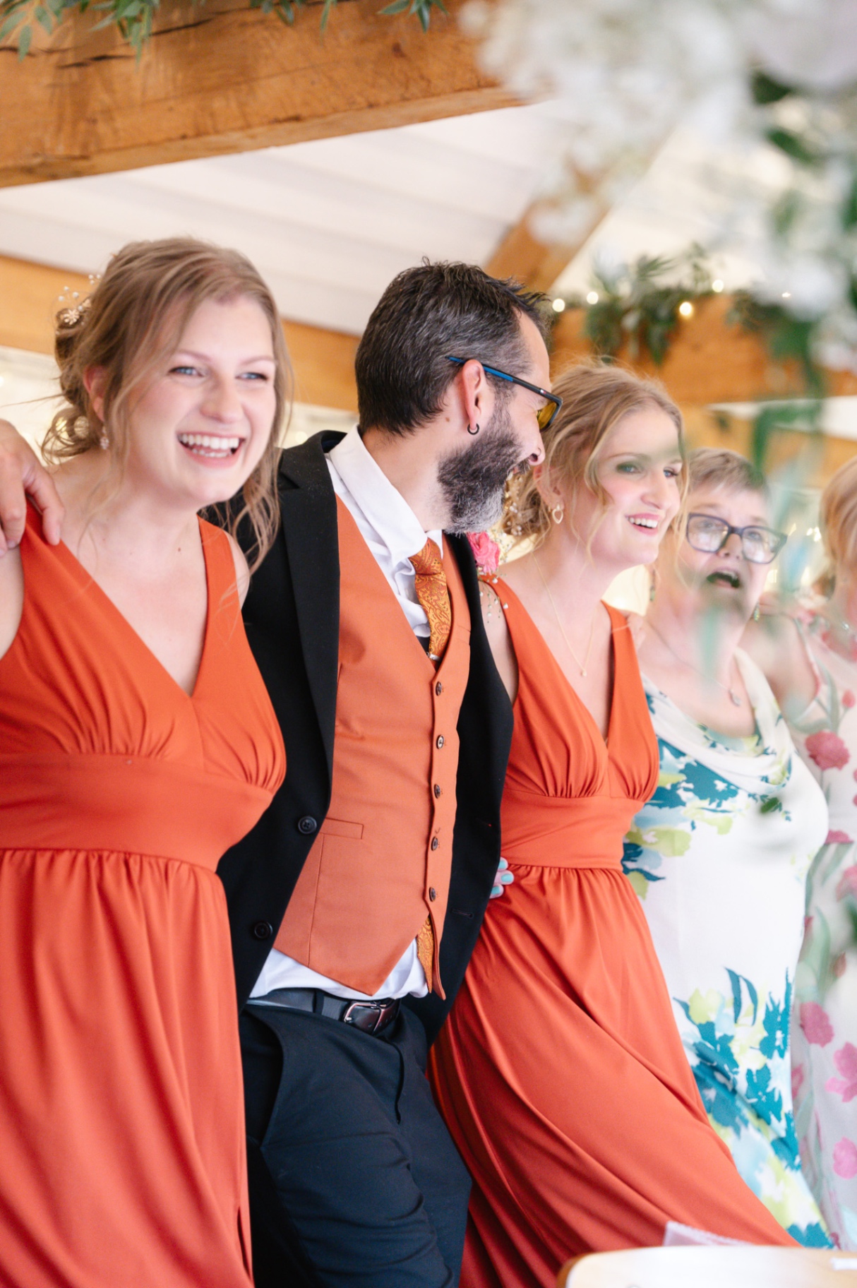 Bridal party laughing together in coral dresses during the reception, wedding photography Worcestershire & Midlands