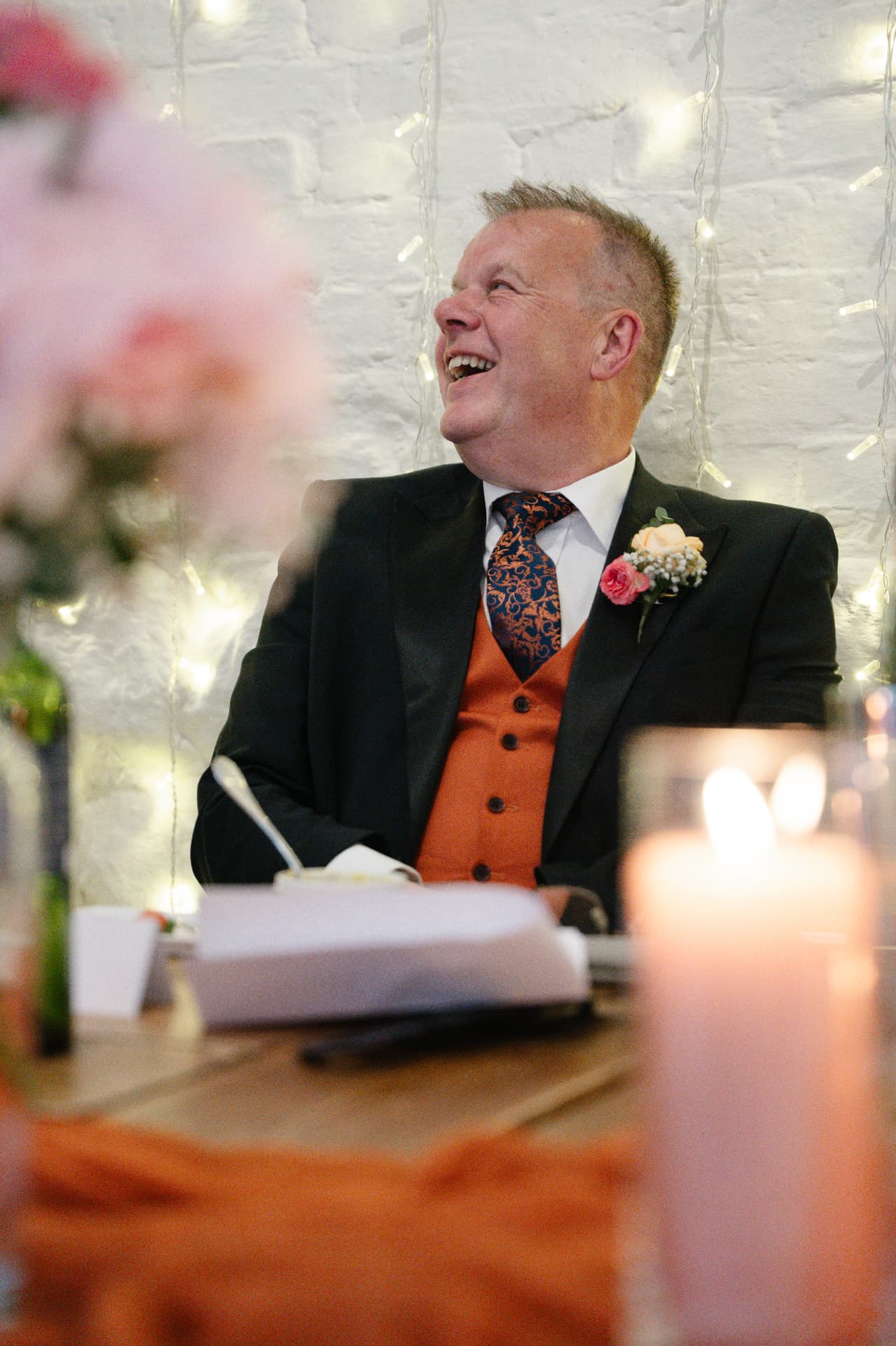 Wedding guest laughing during the speeches in a candlelit barn, wedding photography Worcestershire & Midlands