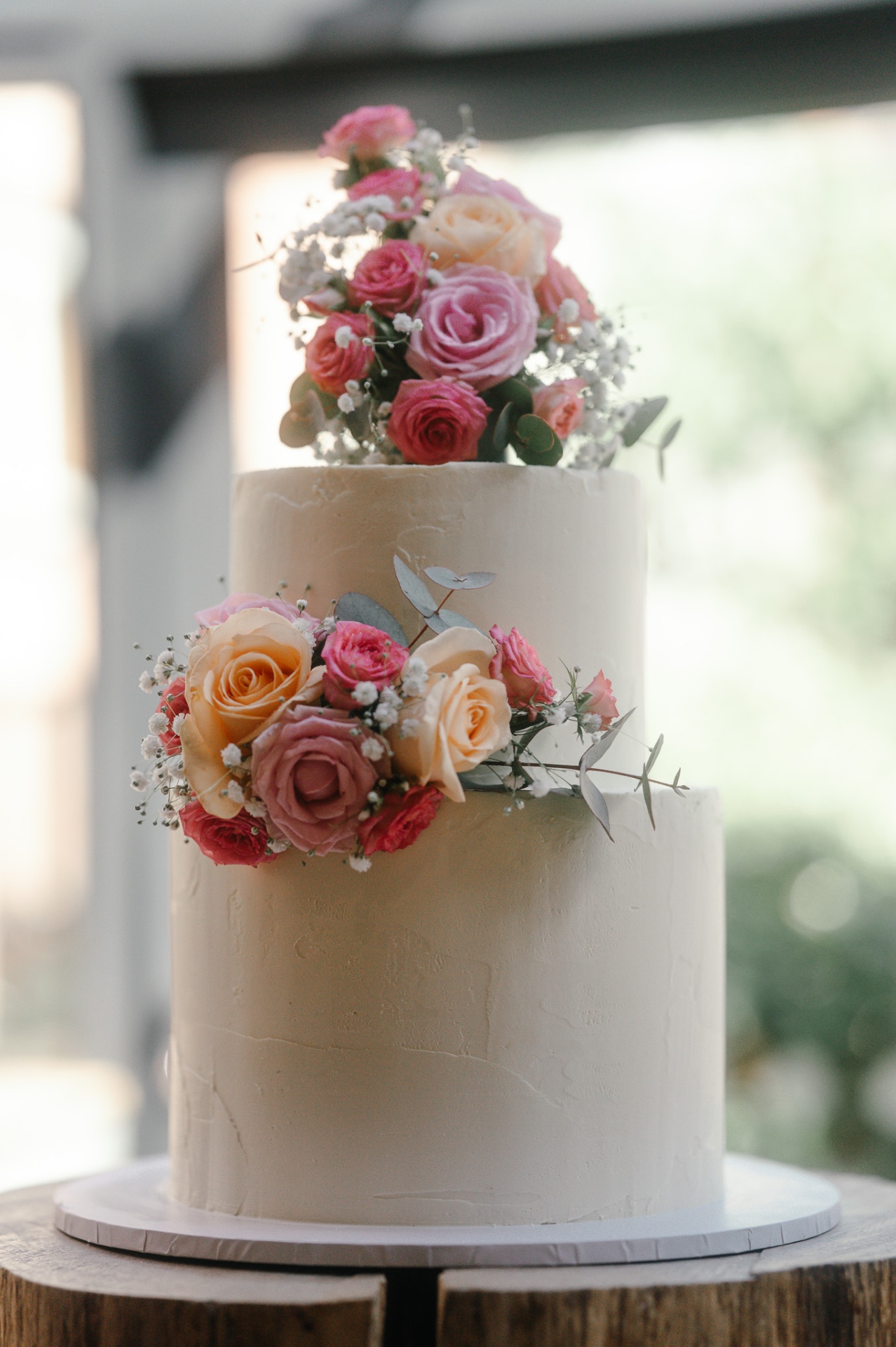Two-tier white wedding cake topped with pink and peach roses