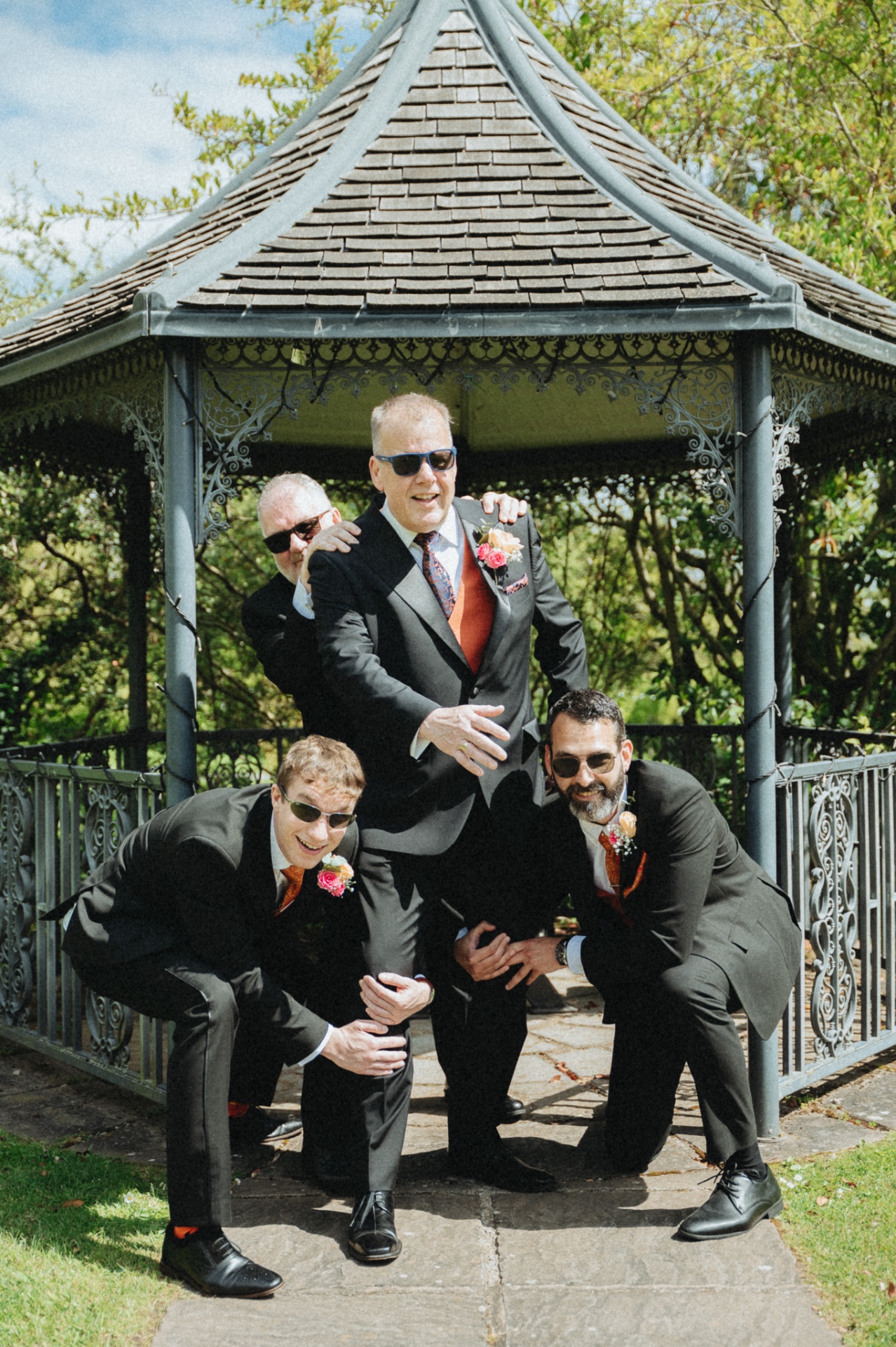 Groom and groomsmen posing playfully under a Victorian bandstand, wedding photography Worcestershire & Midlands