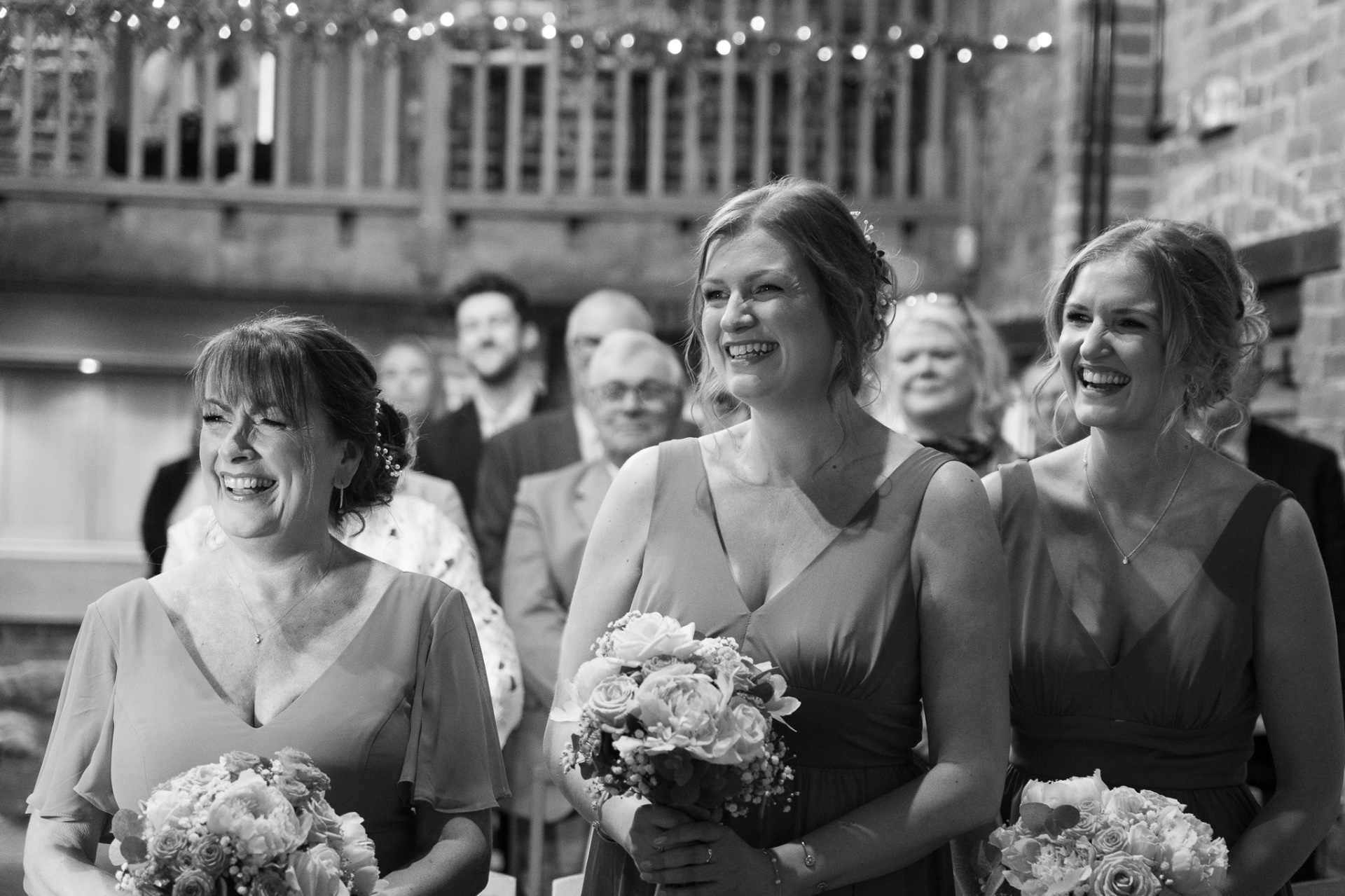 Black and white candid of bridesmaids laughing together during the ceremony