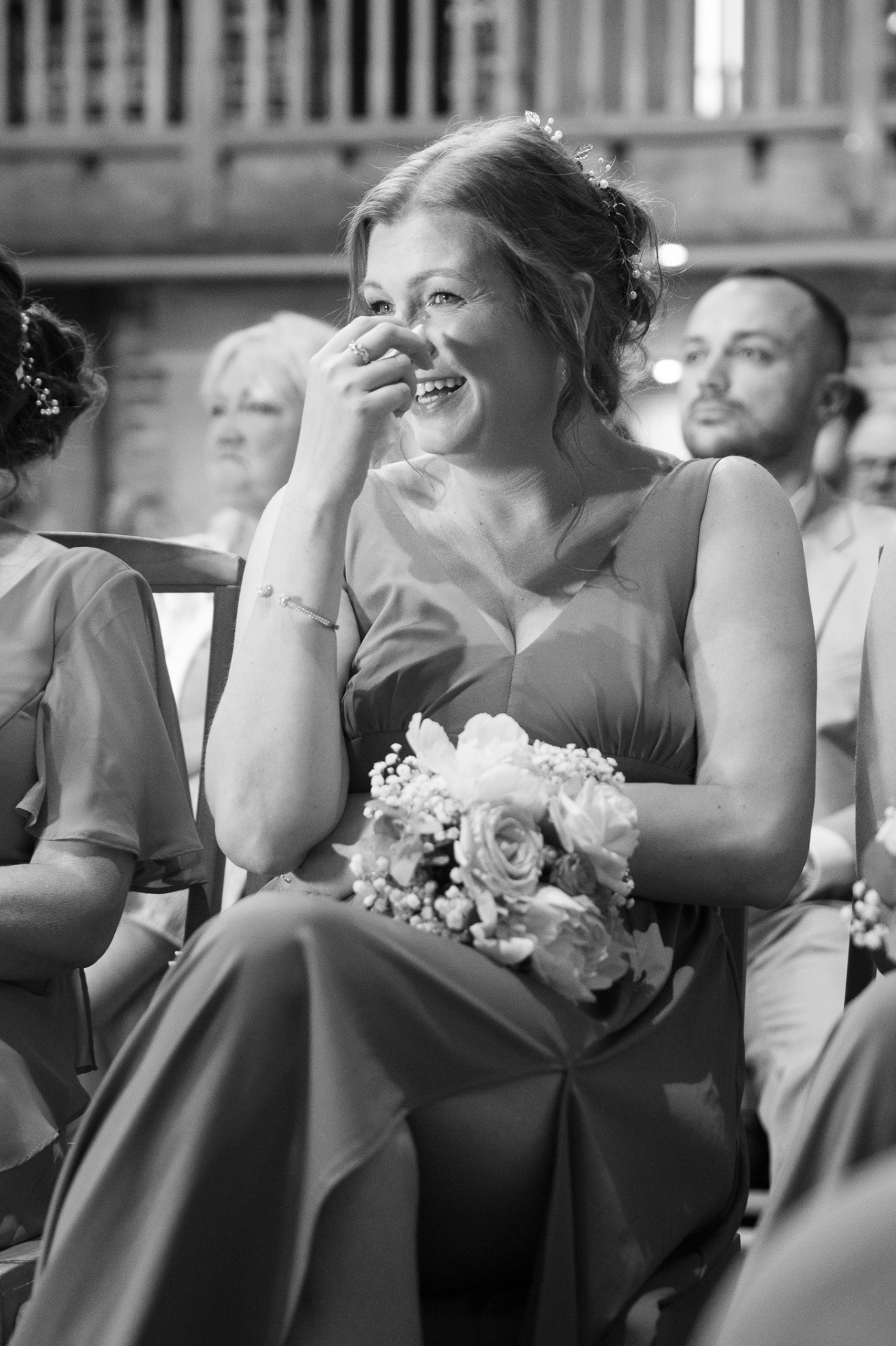 Black and white candid of a bridesmaid laughing during the ceremony, wedding photography Worcestershire & Midlands