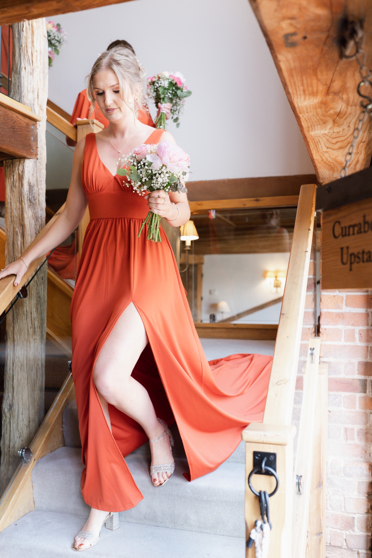 Bridesmaid in a flowing terracotta dress on the wooden staircase at Curradine Barns
