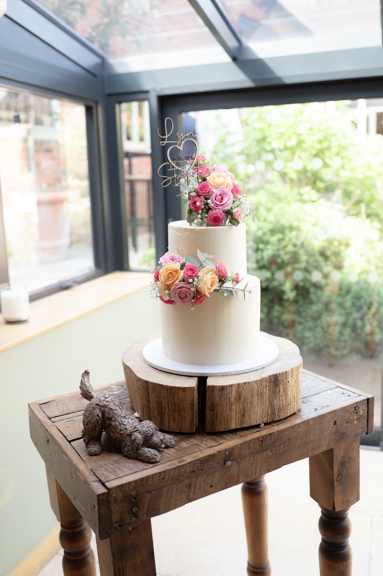 Wedding cake with pink and peach roses and a custom Lyn & Stu topper in a conservatory, wedding photography Worcestershire & Midlands