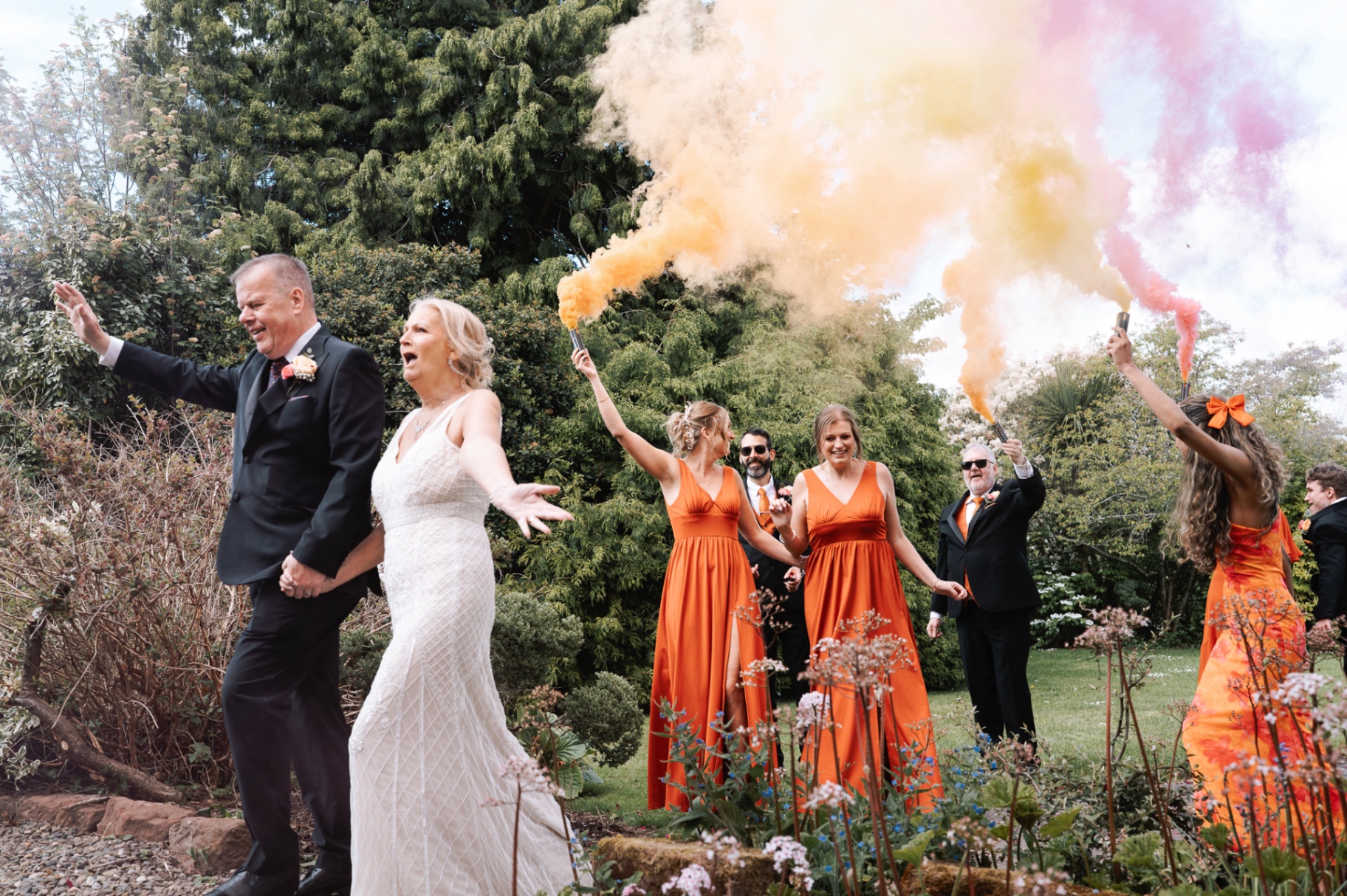 Bride and groom celebrating with orange and pink smoke bombs in the gardens